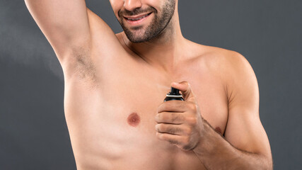 Closeup of young man spraying deodorant for body freshness and hygiene in gray studio banner background