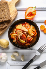 Black bowl with delicious beef stew and different ingredients on white background
