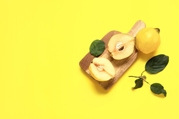 Wooden board with halves of sweet ripe quince and leaves on yellow background