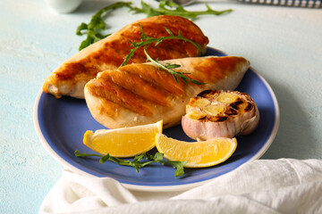Plate of tasty grilled chicken breast with garlic, arugula and lemon on light blue background