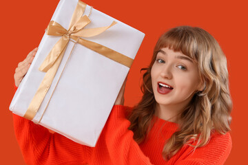 Beautiful shocked young woman with gift box on orange background