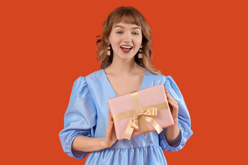 Beautiful young woman with gift box on orange background