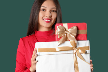 Beautiful young Asian woman with gift boxes on green background