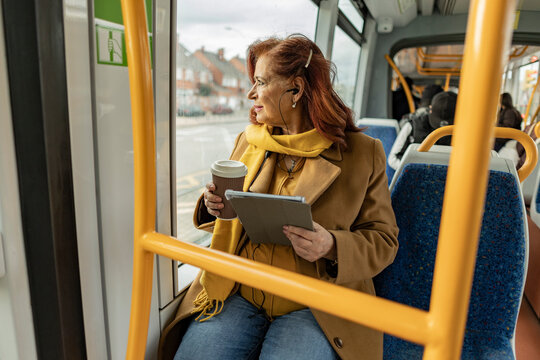 Woman commuting by bus listening to music and drinking coffee