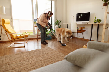 Woman vacuuming living room with dog and headphones