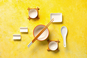 Bowl with chopsticks, cups and spoon on yellow grunge background, closeup. Chinese table setting