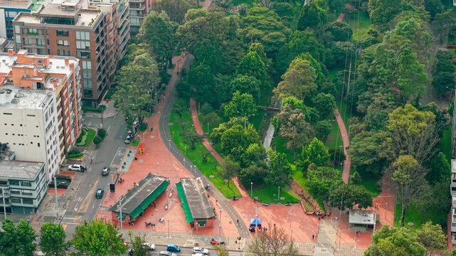 Side drone view of Parque 93, Bogot&aacute;, showing orange ground, trees, people, and surrounding buildings.