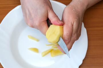 Hands skillfully peeling a fresh potato in a cozy kitchen setting