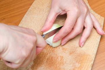 Hands skillfully slicing an onion on a wooden cutting board