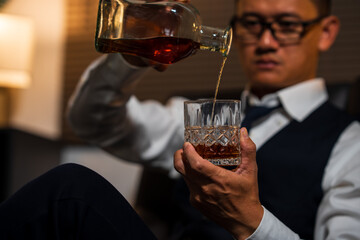Businessman holding a glass of whiskey, sitting and drinking in a room