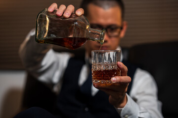 Businessman holding a glass of whiskey, sitting and drinking in a room