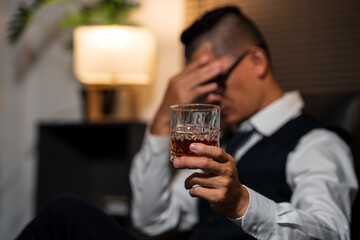 Businessman holding a glass of whiskey, sitting and drinking in a room