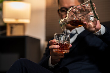 Businessman holding a glass of whiskey, sitting and drinking in a room