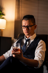 Businessman holding a glass of whiskey, sitting and drinking in a room