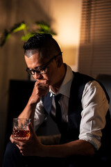 Businessman holding a glass of whiskey, sitting and drinking in a room