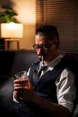 Businessman holding a glass of whiskey, sitting and drinking in a room