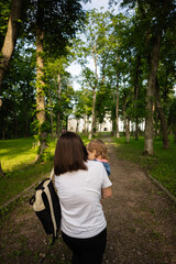 Naklejka premium Mother and child walking through lush green park towards historic building