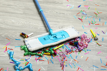Mop with confetti on light wooden floor after party, closeup