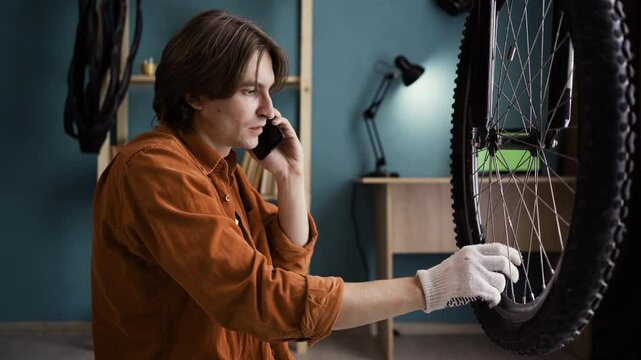 Young Man Sitting by Broken Bicycle Wheel at Home Calling Mechanic About Flat Tire