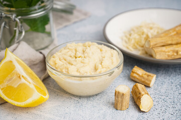 Horseradish sauce in glass bowl with lemon and horseradish roots on white background