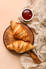 Wooden board with tasty croissants and bowl with jam on brown background