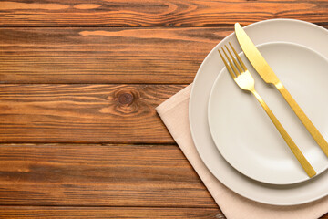 Beautiful table setting with plates and golden cutlery on wooden background