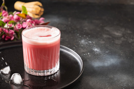 Pink matcha latte with powder decorated sakura flowers on dark background. Trendy beverage. Refreshing iced pink matcha. Close up.