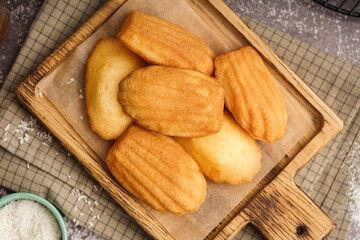 Wooden board with madeleines on grey background