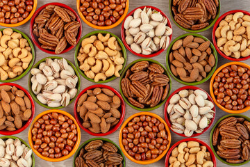 Pattern of various types of nuts in multi-colored round ceramic bowls on a wooden texture table, top view. The concept of healthy eating and healthy living,