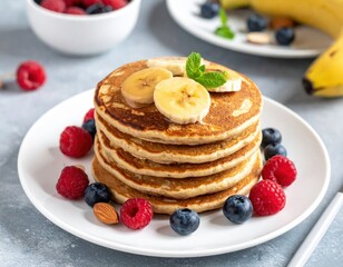 Stack of pancakes with banana slices and fresh berries sits on a white plate ready to be eaten for breakfast or brunch, it is a tasty and healthy meal.
