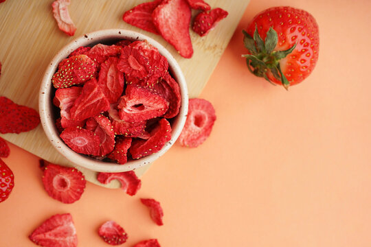 Bowl with tasty freeze-dried strawberries on orange background