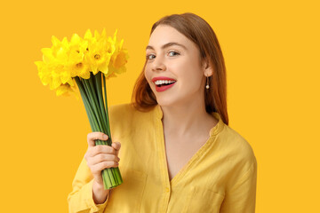 Happy young woman with bouquet of beautiful daffodil flowers on yellow background