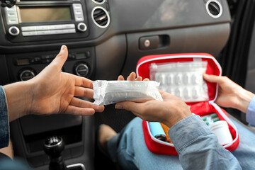 Woman passing bandages from first aid kit to male driver in car