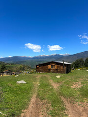 A wooden cabin with Snow-Capped Peaks in the mountains on a sunny day. Rustic Cabin. Scenic view of rolling hills, mountains, and a cloudy sky under sunlight.