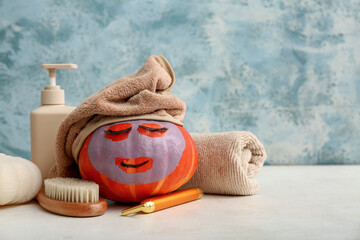 Funny pumpkin with false eyelashes, cosmetic mask and bath supplies on light table against color...