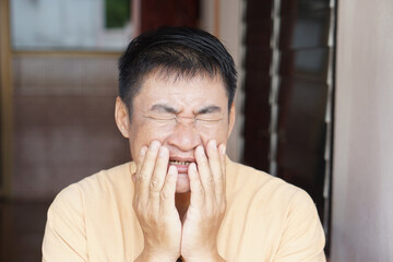 A middle-aged Asian man suffering from a severe toothache. His painful facial expression and hand...