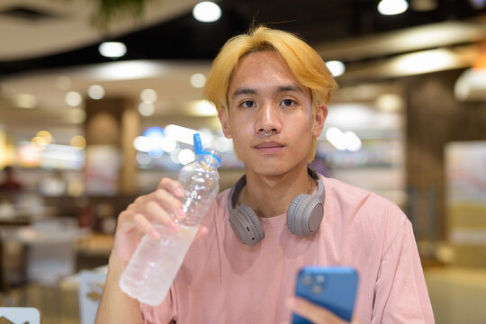 Young student teenager man with headphones drinking water and using mobile phone