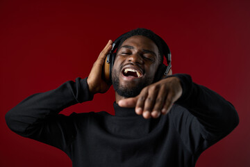 Young Black man enjoying music with headphones, smiling and dancing against a vibrant red background, capturing joyfulness and rhythm in a modern style
