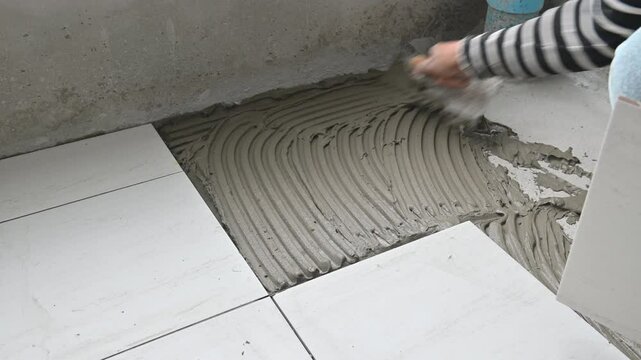 4K Worker applies cement adhesive to the floor for laying floor tiles