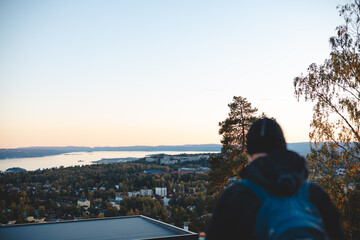 Overlooking Oslo from above, a traveler watches the sunset paint the horizon in peach and blue, embracing a serene Scandinavian evening from the heights