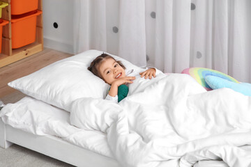 Cute little girl in pajamas lying in bed in children's room