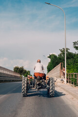 A farmer from behind slowly drives an old tractor across a bridge, typical of a late summer afternoon, and conveys a sense of homecoming after a long day of work in the fields.