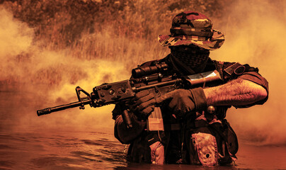Soldier in camouflage, face covered, holding rifle in water with thick smoke behind.
