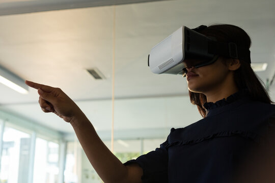 Person wearing VR headset is pointing forward in modern glass office with fluorescent lighting