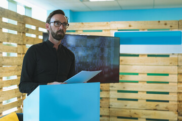 Blue podium standing in conference room with windows against wooden wall with flat-screen display