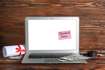 Modern laptop with text STUDENT LOAN, money, diploma and small graduation hat on wooden background