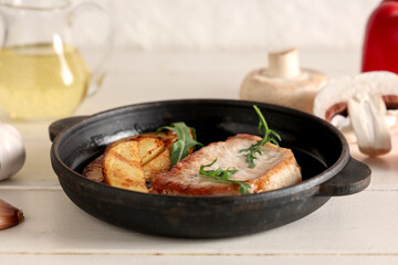 Frying pan with roasted steak and potato on white wooden table