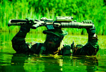 Camouflaged soldier in aquatic setting holding a rifle above head while partially submerged in water amidst lush greenery.