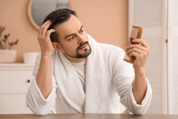 Worried young man with hair loss problem and comb in bathroom