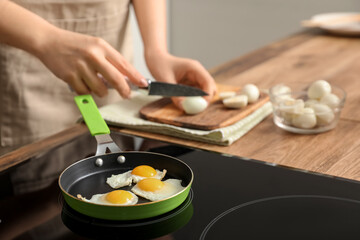 Woman frying quail eggs on electric stove in kitchen, closeup
